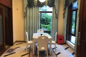 Uma área de refeições com uma mesa e cadeiras brancas, um banquinho vermelho pequeno e um tapete estampado.