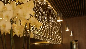 A modern bar area with a wooden ceiling, a decorative wall with geometric patterns, and a white vase with orchids. - ASBU Hotel (Tunis)