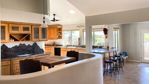 A modern kitchen with wooden cabinets, a granite countertop, and a curved island with seating. - Songbirds N Serenity (Oro Valley)