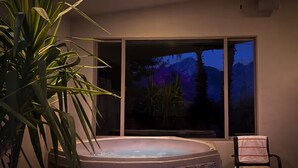 A hot tub with a stone facade, a chair, and a view of a mountain range at dusk. - Songbirds N Serenity (Oro Valley)