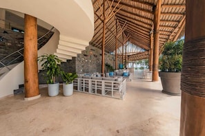 Un hall d’entrée spacieux avec un escalier en colimaçon, un coin salon avec des coussins et de grandes plantes en pot.