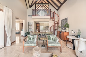 Relax in a spacious living area with a high ceiling and exposed beams, featuring a central seating area with sofas and a dining space.