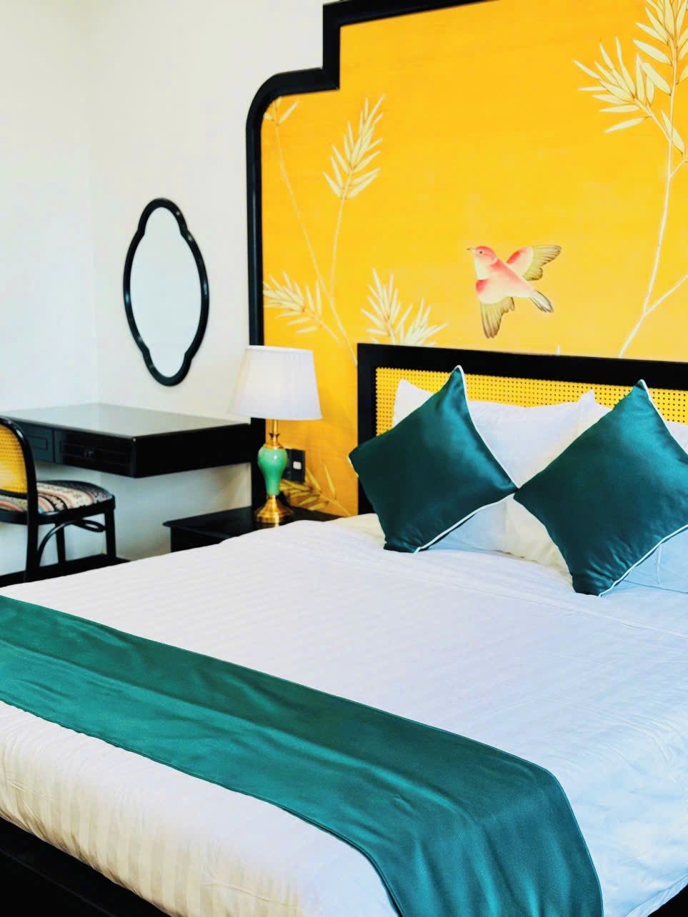 A hotel room with a bed, a desk, a chair, and a nightstand with a lamp.