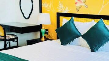 A hotel room with a bed, a desk, a chair, and a nightstand with a lamp.