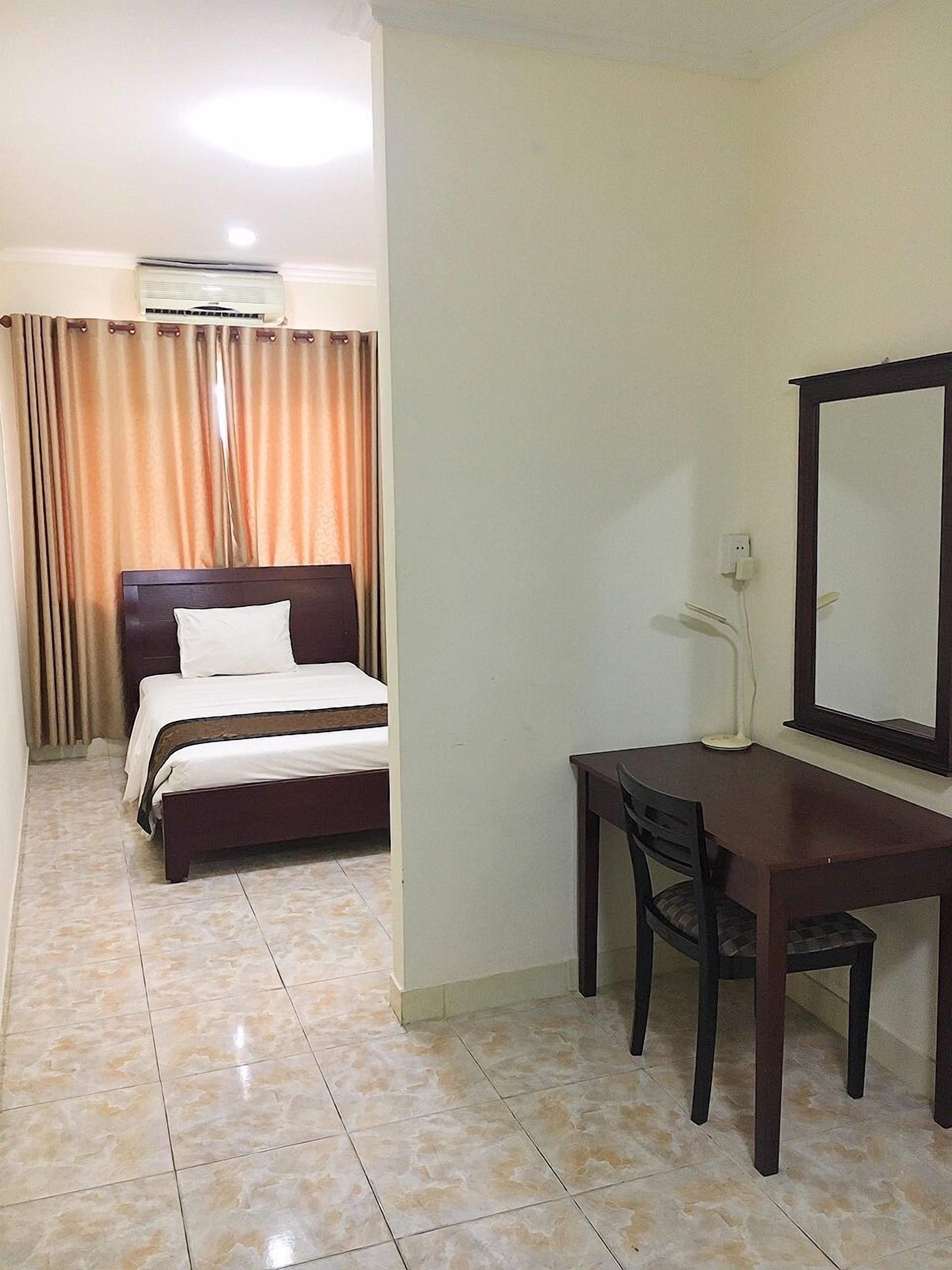 Una habitación de hotel con cama, escritorio, silla, espejo y aire acondicionado.