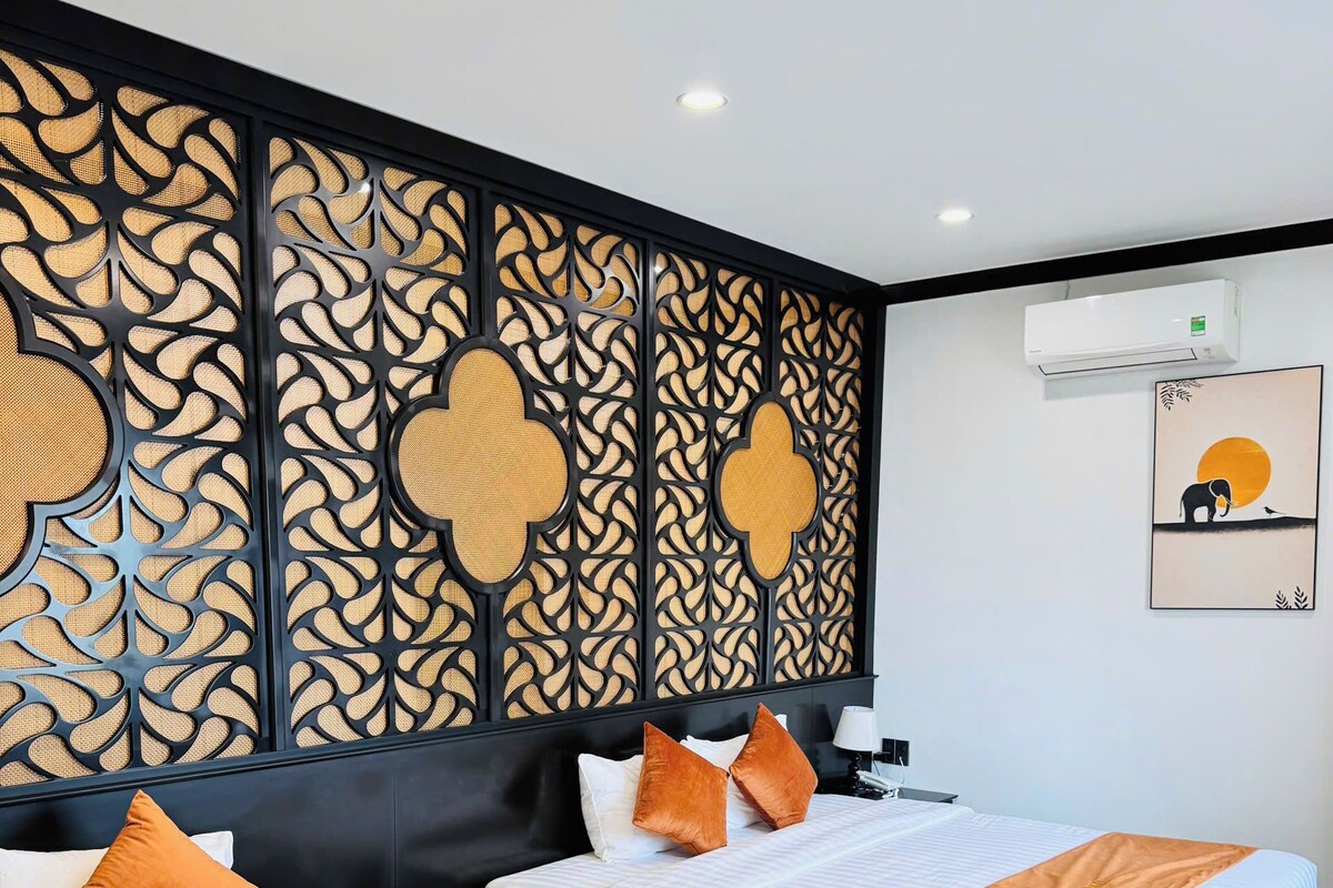 Een hotelkamer met twee bedden, een decoratief paneel, een airconditioning en een ingelijste foto aan de muur.