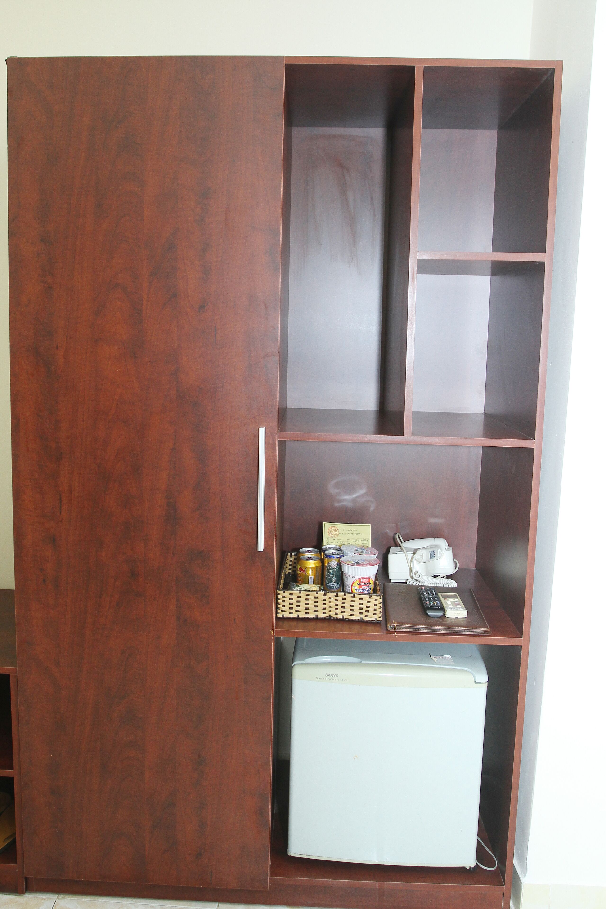 A wooden wardrobe with multiple compartments, a small refrigerator, and a few items on the top shelf.