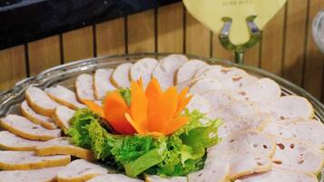 A glass platter with sliced meat arranged in a circular pattern, garnished with lettuce and orange carrot flowers, set on a green cloth.
