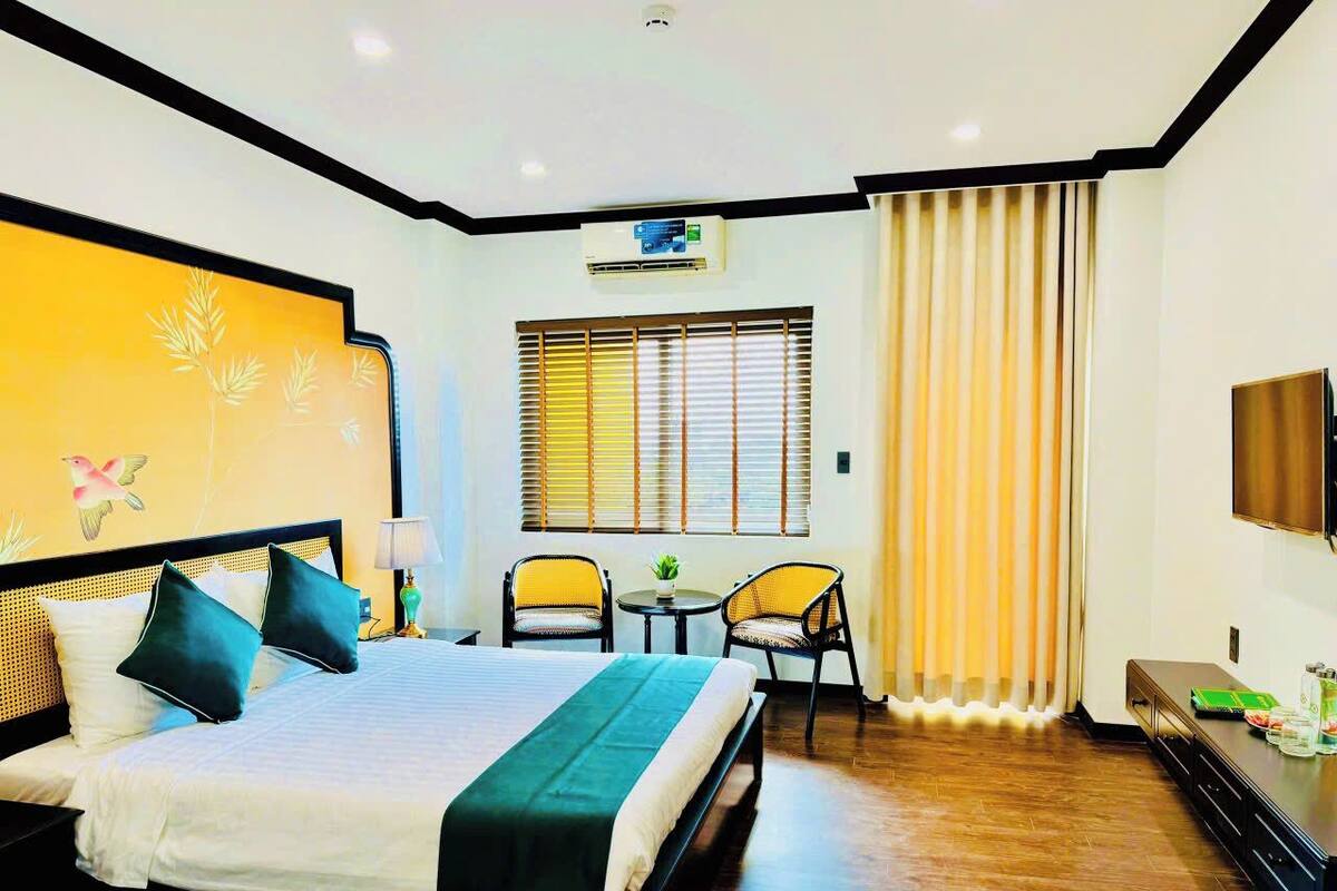 Een hotelkamer met een bed, twee stoelen, een tafeltje, een televisie en een raam met luxaflex.
