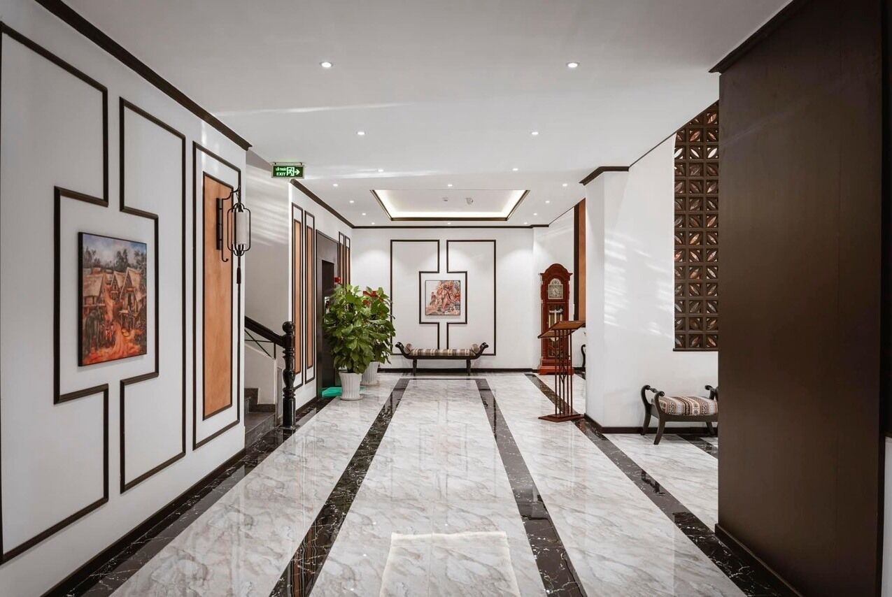 A hotel lobby with a marble floor, framed artwork on the walls, a bench, and a potted plant.