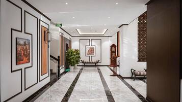 A hotel lobby with a marble floor, framed artwork on the walls, a bench, and a potted plant.