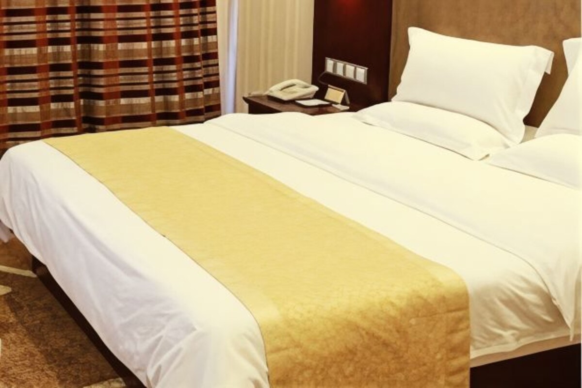 A hotel room with a large bed, a bedside table with a phone, and a window with curtains.