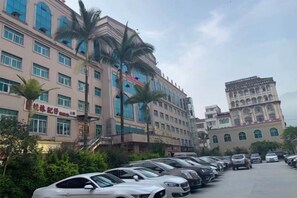 A parking lot with multiple cars, a building with a traditional architectural style, and palm trees. - Wuji Hotel (Tian'e)