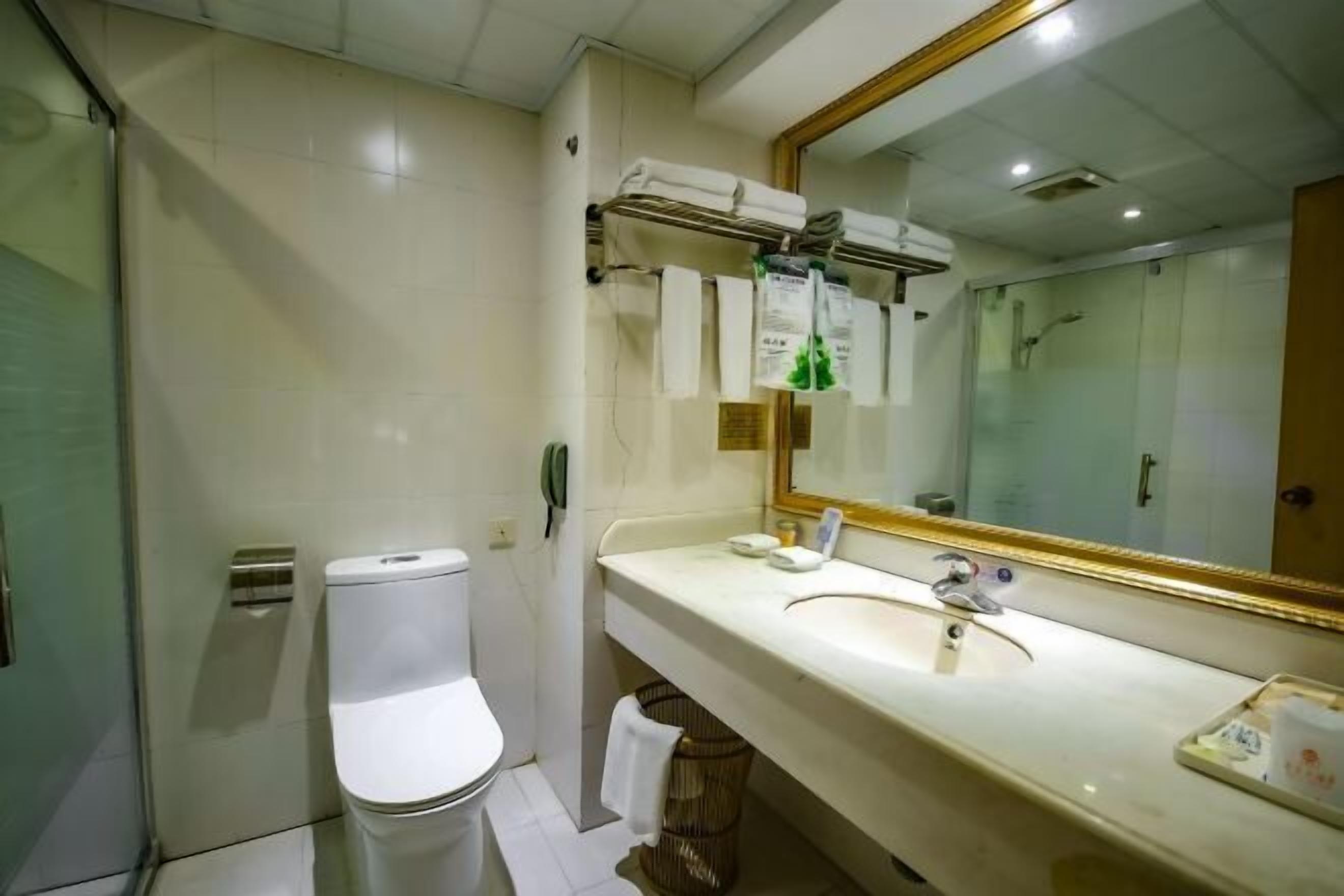 A bathroom with a toilet, sink, and mirror. There are towels hanging on a rack and a basket under the sink.