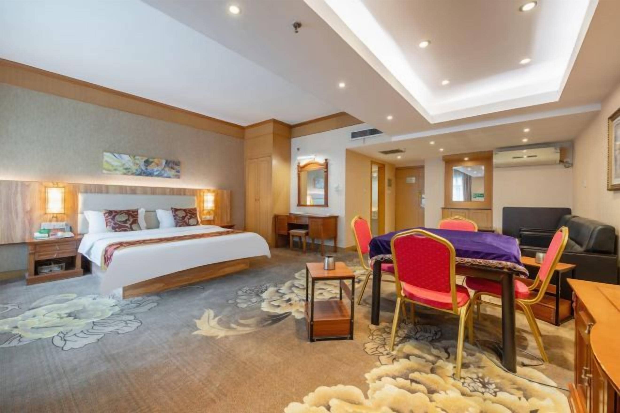 A hotel room with a bed, desk, chairs, and a television.