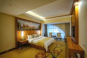 Una habitación de hotel con una cama, un escritorio, una silla, un televisor y un cuadro en la pared.