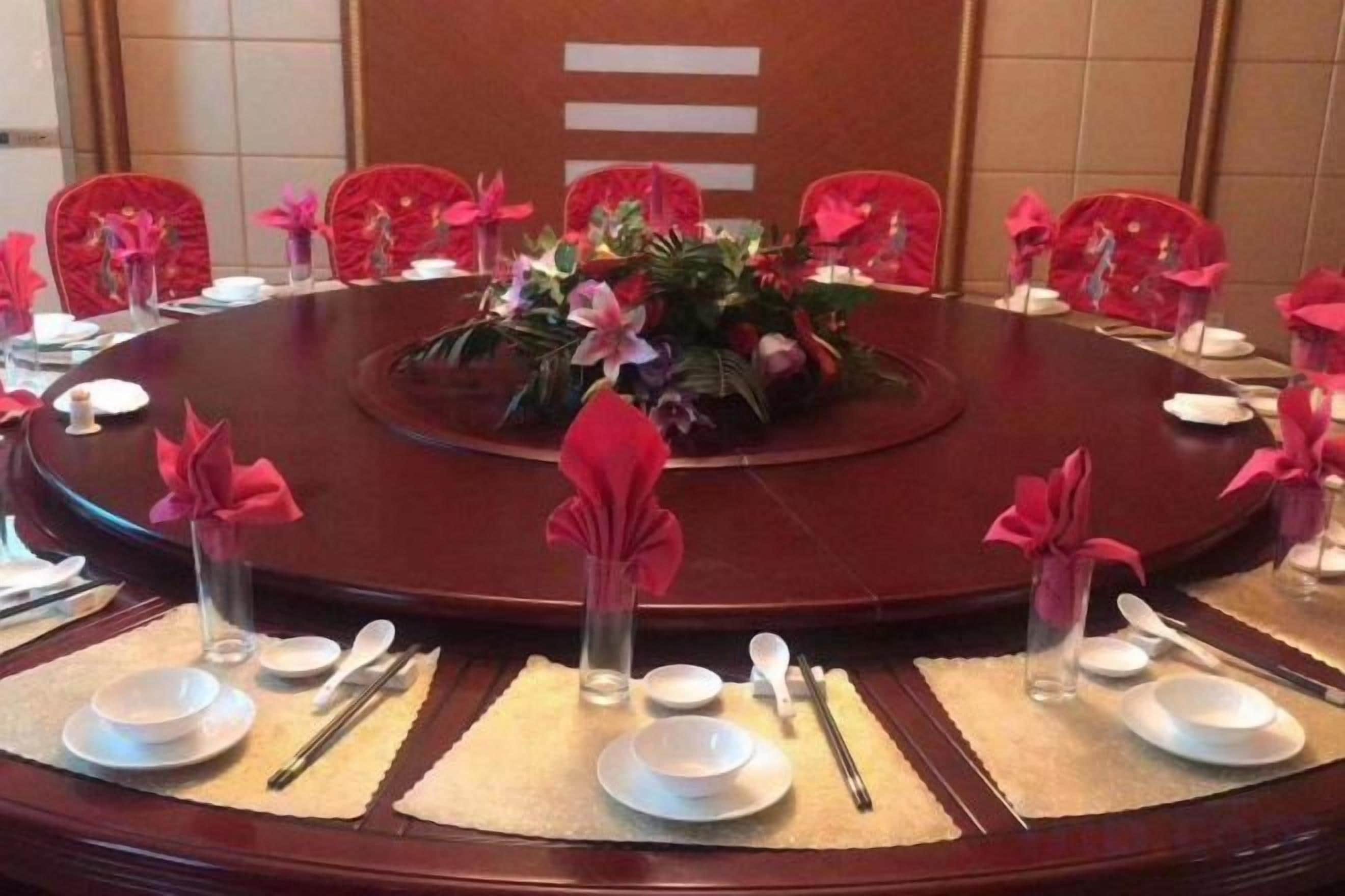 A round table set for a meeting with red chairs, white plates, and silverware.