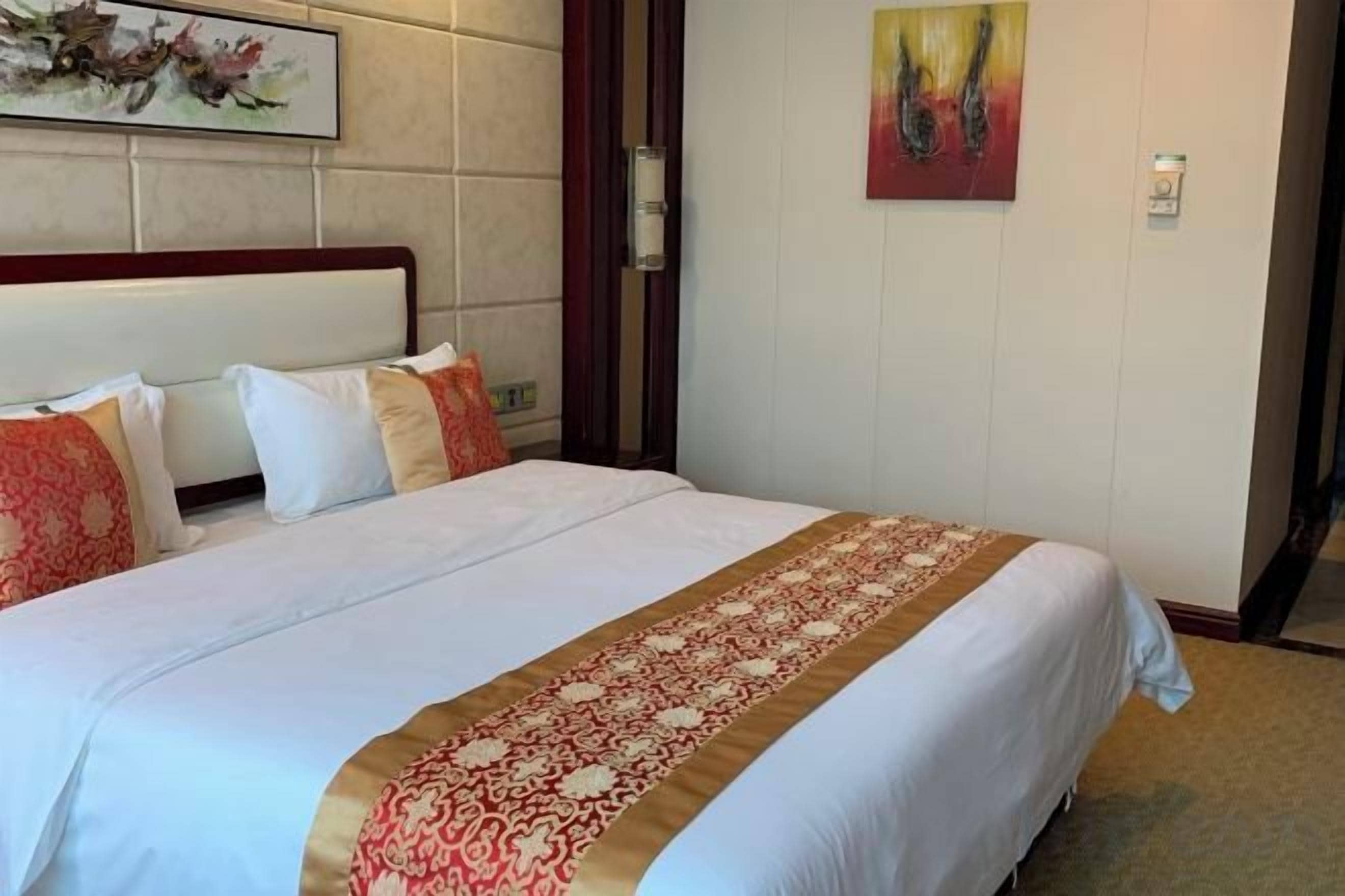 A hotel room with a large bed, a headboard, and a painting on the wall.