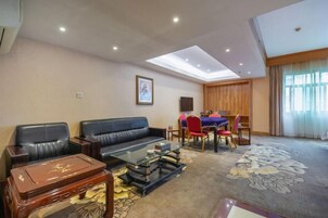 Habitación de hotel con sofá, mesa de centro, mesa de comedor con sillas y un ventanal grande.