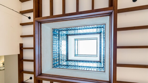 A framed view of a spiral staircase with a glass railing, wooden beams, and a light fixture on the left. - San Marcos. 2 bedrooms, 2 bathrooms (Sevilla)