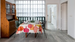 A dining area with a table set for four, a wooden cabinet with glass doors, and a large window with blinds. - San Marcos. 2 bedrooms, 2 bathrooms (Sevilla)