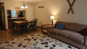 Uma sala de estar aconchegante com um sofá, uma mesa de centro e um espaço de refeições com cadeiras e mesa.