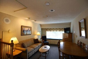 Ein Zimmer mit einer Couch, einem Esstisch, einem Fernseher und einem Fenster mit Blick.