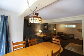 Relax in this inviting living room with a dining area, featuring a wooden dining table, comfortable sofa, and unique pendant light.