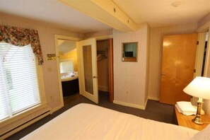 Ein Hotelzimmer mit Bett, Nachttisch mit Lampe, Spiegel, Schrank und einem Badezimmer mit Waschbecken.