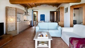 A cozy living area with a sofa, a coffee table, a TV, and a kitchen in the background. - Apartment "Ida Isuledda 2" with Pool, Garden & Wi-Fi (San Teodoro)