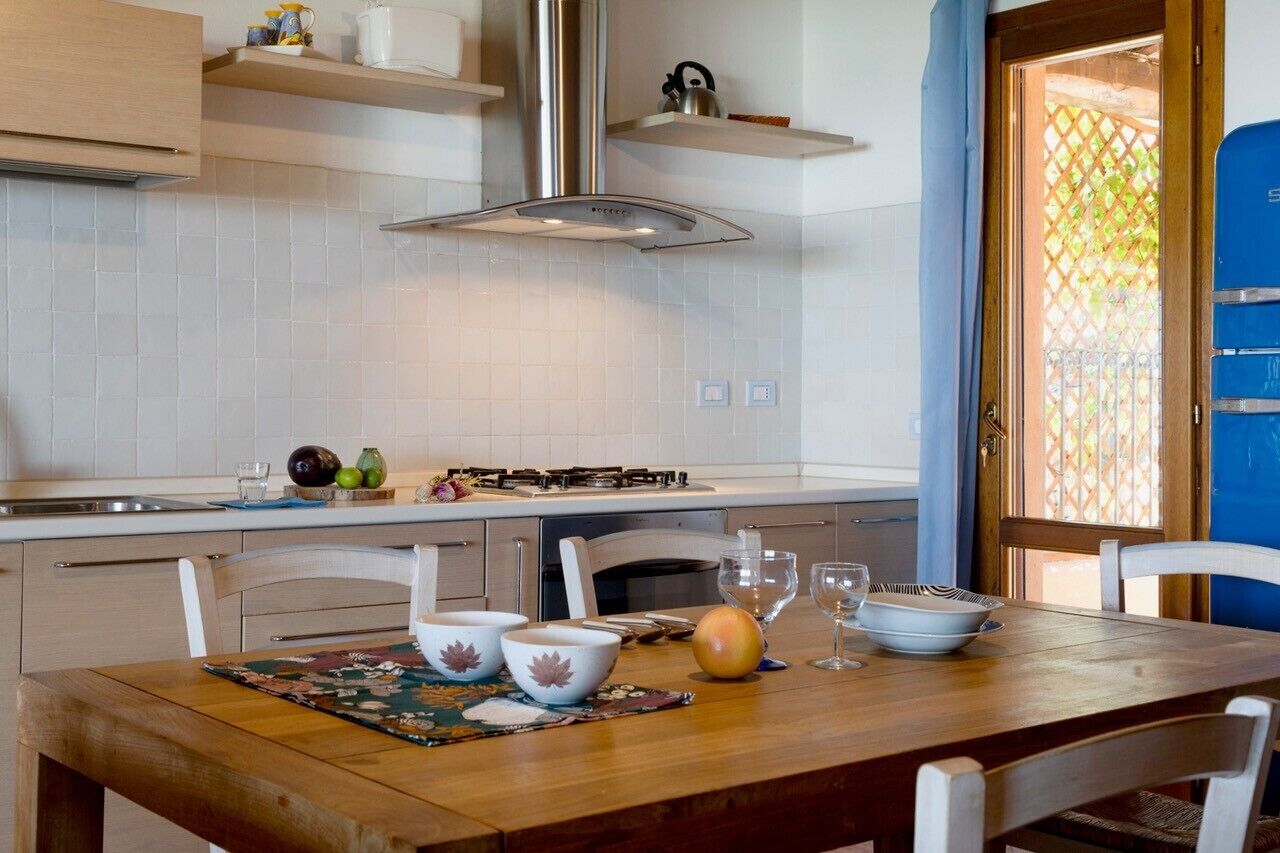 A kitchen with white cabinets, a stainless steel range hood, and a dining area with a wooden table and white chairs.