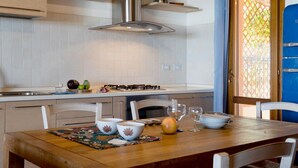 A kitchen with white cabinets, a stainless steel range hood, and a dining area with a wooden table and white chairs. - Apartment "Ida Isuledda 2" with Pool, Garden & Wi-Fi (San Teodoro)
