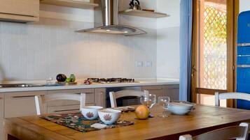 A kitchen with white cabinets, a stainless steel range hood, and a dining area with a wooden table and white chairs.