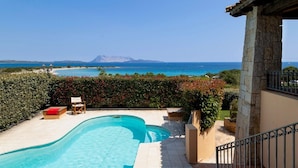 A swimming pool with a view of the sea and mountains, a stone pillar, and a chair. - Apartment "Ida Isuledda 2" with Pool, Garden & Wi-Fi (San Teodoro)