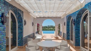 Un espace extérieur aménagé, abrité et doté de sièges, avec vue sur la piscine, du mobilier blanc et des murs recouverts de carreaux bleus.