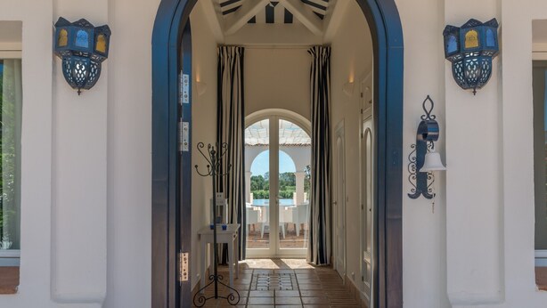 Un couloir doté d’une entrée en arc de cercle, de deux portes-fenêtres et de deux lanternes fixées aux murs.