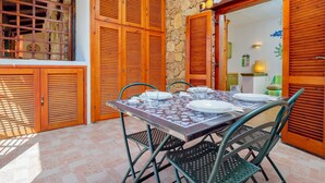 Un coin repas avec une table dressée pour quatre personnes, entouré de volets en bois et de murs en pierre.