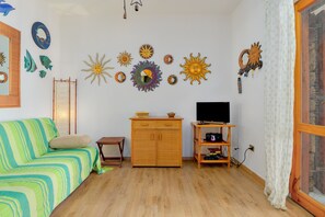 A room with a green-striped sofa, a wooden cabinet, a TV on a wooden stand, and wall decorations including sun motifs.