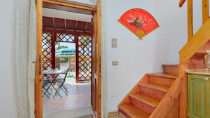 Un escalier en bois menant à une porte verte, un coin repas avec une table et des chaises, et un ventilateur rouge fixé au mur.