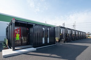 A modern building with a green and white facade, large glass doors, and a series of shipping containers in the background.