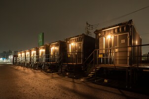 Una fila de vagones de tren adaptados como habitaciones de hotel, con escaleras exteriores y un cartel verde al fondo.