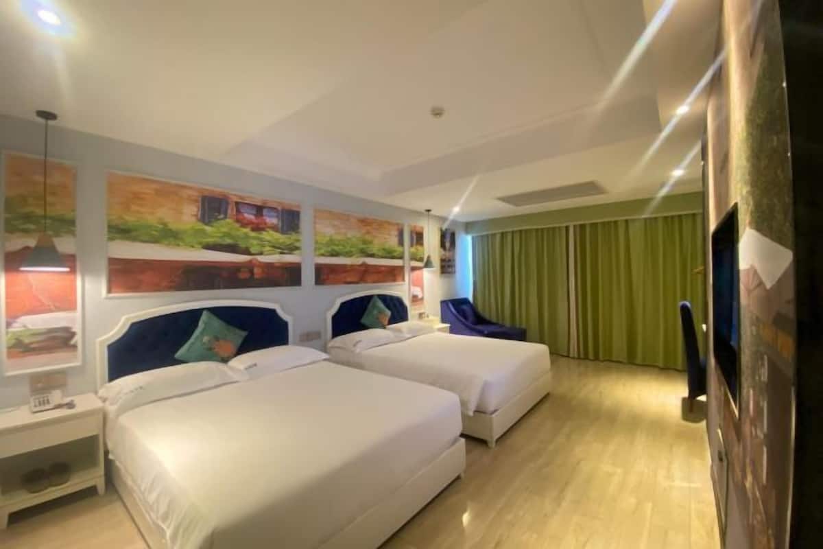 Ein Hotelzimmer mit zwei Betten, einem grünen Vorhang und einer Wand mit drei Bildern.