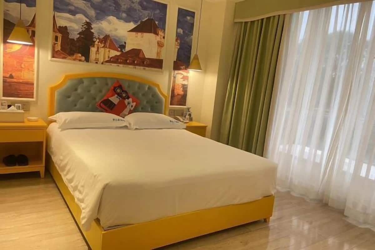 Ein Hotelzimmer mit Bett, Nachttisch, Lampe und einem Fenster mit Vorhängen.
