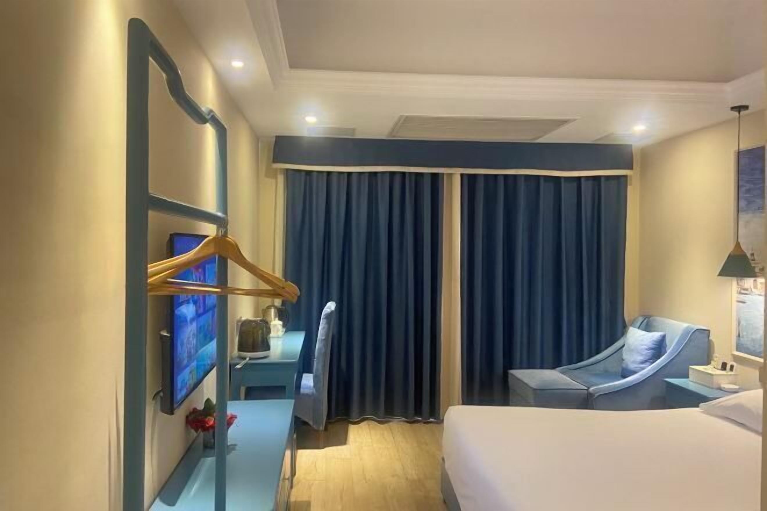 Una habitación de hotel con cama, escritorio con computadora, silla y televisor montado en la pared.