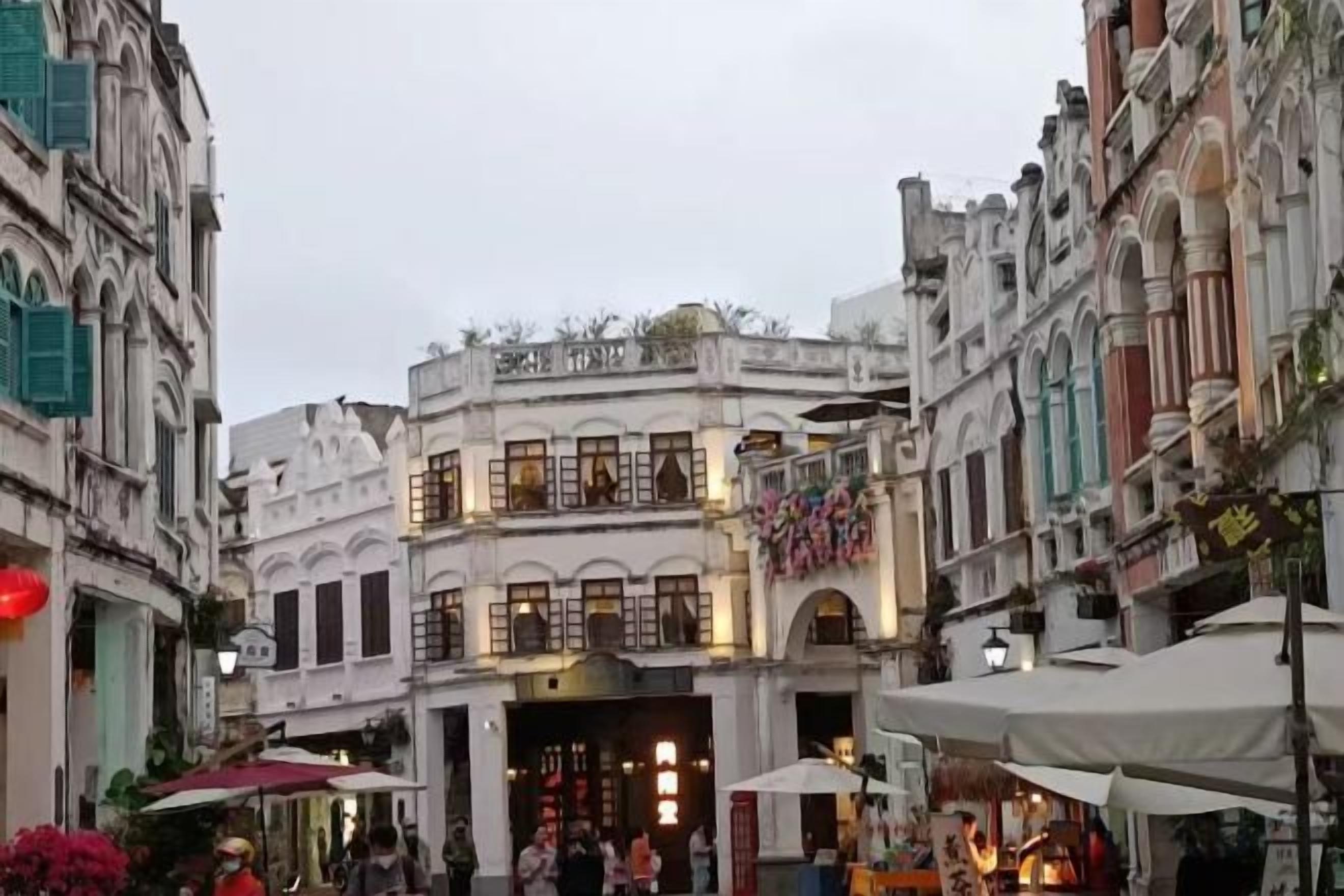 Une rue bordée d’immeubles, dont certains sont dotés d’auvents et d’enseignes, et où l’on voit quelques personnes se promener.