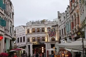Una calle con edificios, algunos con toldos y letreros, y algunas personas caminando.