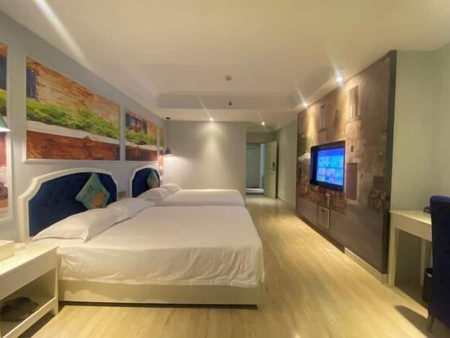 A hotel room with a large bed, a TV on the wall, and artwork on the walls.
