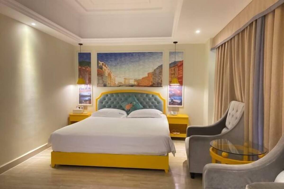 Ein Hotelzimmer mit einem großen Bett, zwei Nachttischen, einem Sessel und einem Glastisch.
