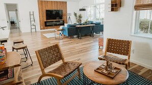 A spacious living room with a wooden floor, a TV mounted on a wooden wall, a blue sofa, and a coffee table with a board game. - Sunset Glow *Hidden Meadow*BBQ HotTub by Casa Oso (Oakhurst)