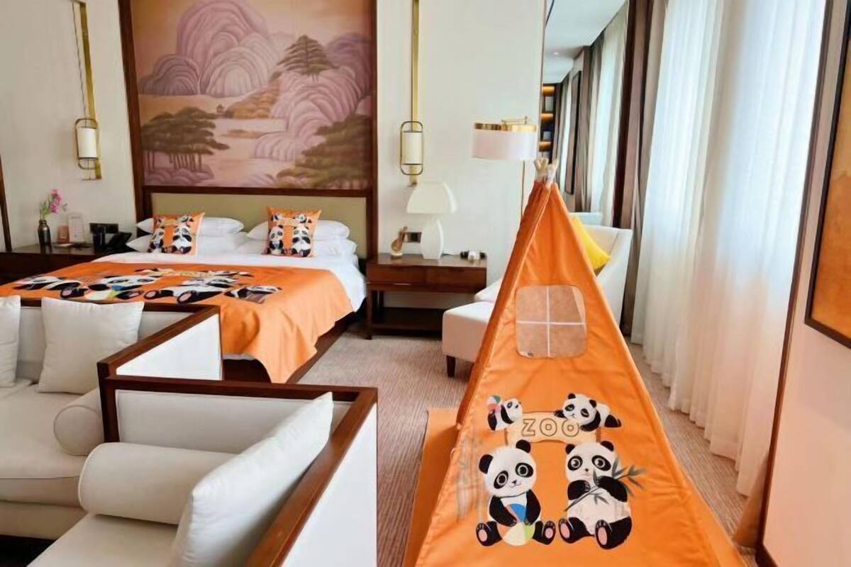 Una habitación de hotel con una cama, dos sillones, un sofá, un cuadro y una ventana con cortinas.